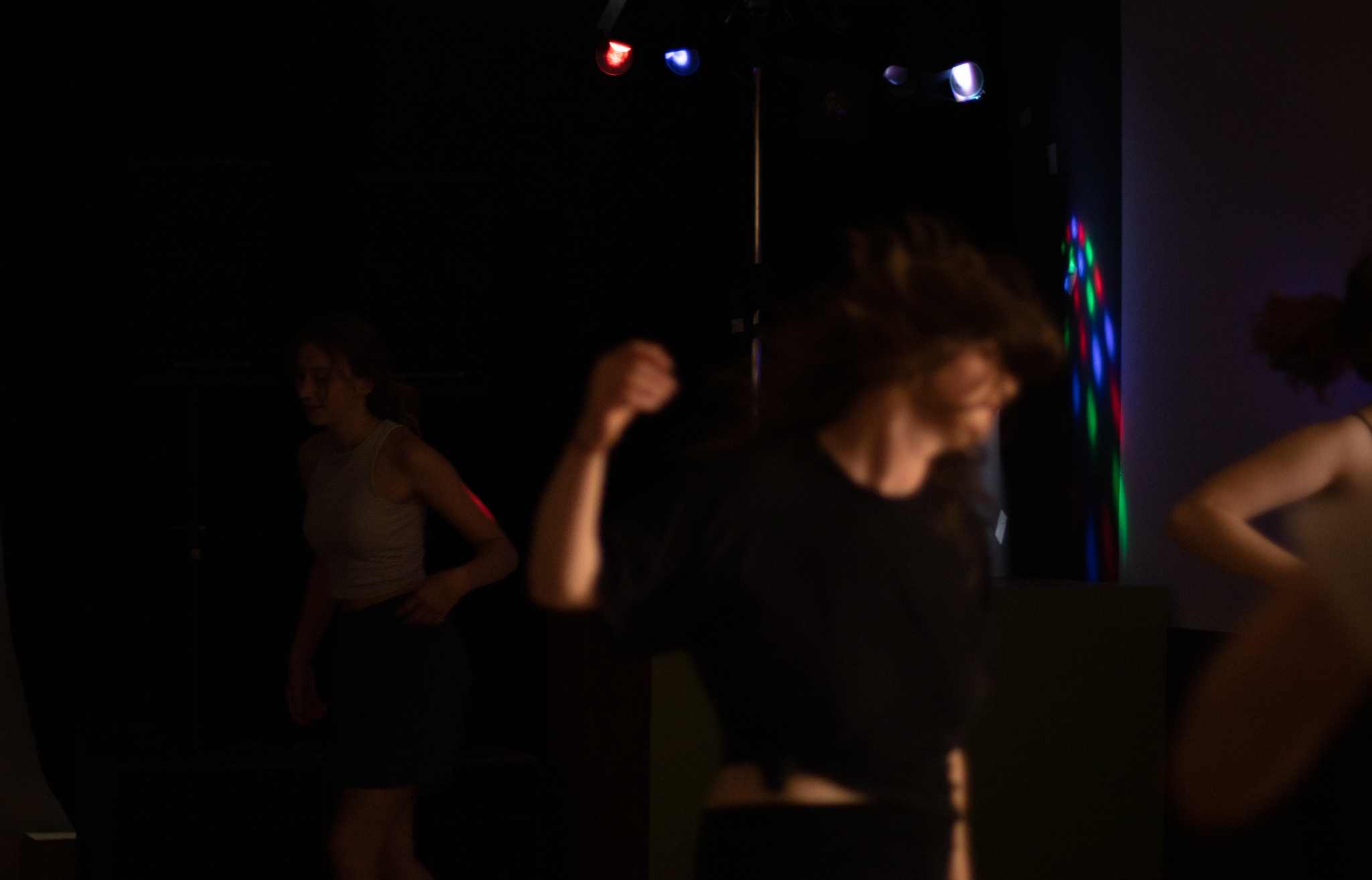 Tanzende Personen in einem dunklen Raum mit bunter Beleuchtung.